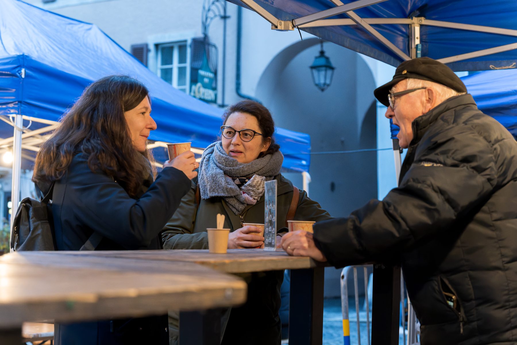 Trois personnes discutent autour d’une table sous les tentes du First Friday